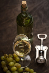 wineglass with white wine,bottle,steel bottle opener and grapes on brown wood textured table