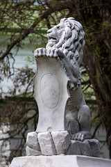 Statue of lion holding a shield in its paws. Regal lion leaning on empty heraldic shield.