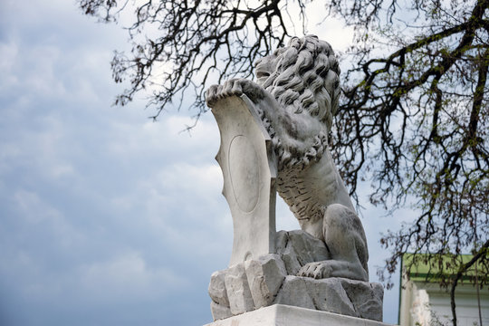 Statue of lion holding a shield in its paws. Regal lion leaning on empty heraldic shield.