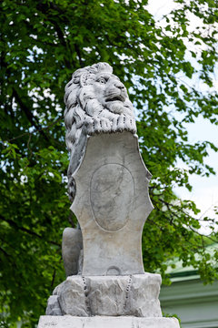 Statue of lion holding a shield in its paws. Regal lion leaning on empty heraldic shield.
