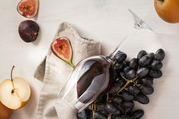 wineglass with red wine,figs,pear apples and black grapes on white wood textured table covered with...