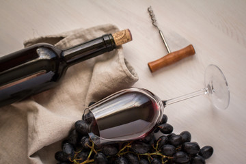 wineglass with red wine with bottle,grapes and old bottle opener on white wood textured table...