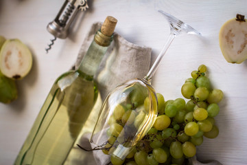 Obraz premium wineglass with white wine with bottle, guava and grapes on white wood textured table covered with canvas towel