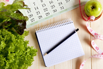 Empty notebook with vegetable salad and apple ,  calendar on wooden table
