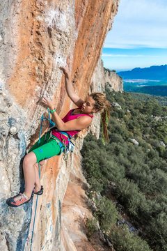 Young Female Climber ascending vertical rocky wall