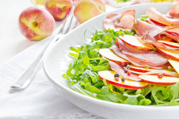Arugula with bresaola and nectarine on white plate
