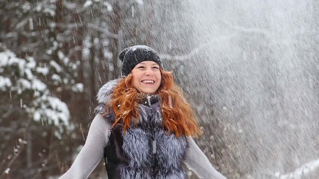 Beautiful young woman having fun outside on winter snowy day. Beauty girl with red long hair enjoying winter day outside. Redhead girl throwing snow up laughing and smiling happily Slow motion video