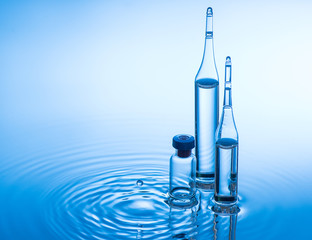 Medical ampoules and bottle on blue water background with splash