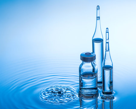 Medical ampoules and bottle on blue water background with splash