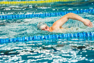 active swimmer performing front crawl freestyle stroke in indoor pool.