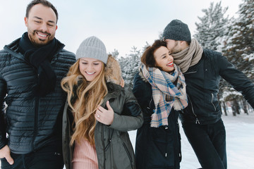 Cute young hipster couples walking in the snow having fun in winter park on a bright day hugging each other and smiling
