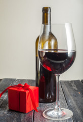 glass of red wine and a gift on a wooden background