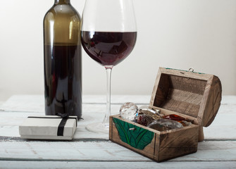 glass of red wine, box with diamonds and a gift on white wooden background, celebration love
