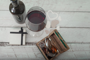 glass of red wine, box with diamonds and a gift on white wooden background, celebration love