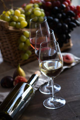 Three wineglasses of red, rose and white wine with bottle, grapes in wicker basket and figs on brown wood textured table covered with canvas towel