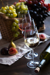 Obraz premium Three wineglasses of red, rose and white wine with bottle, grapes in wicker basket and figs on brown wood textured table covered with canvas towel