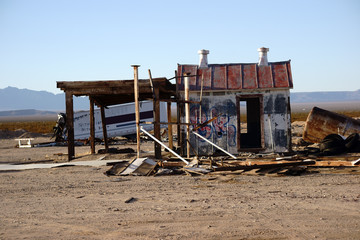 Ruinen in der Ödnis / Verfallene Holzhäuschen, Campinganhänger sowie verrostete Wassertanks in der Ödnis der Wüste.
