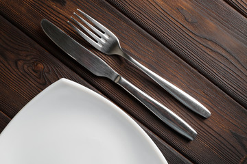 Empty plate, fork and knife on dark wood background