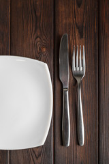 Empty plate, fork and knife on dark wood background