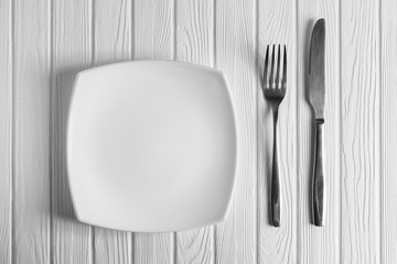 Empty plate, fork and knife on wood background