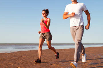 Fototapeta premium Young couple running together beside the water at the beach. Man