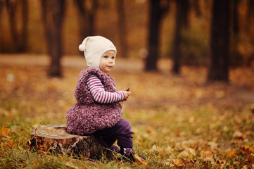 Маленькая девочка сидит на срубе дерева - obrazy, fototapety, plakaty