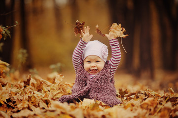 Маленькая девочка играет с листьями в лесу