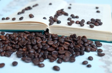 Roasted coffee beans on blurred background of an open book in pastel colours