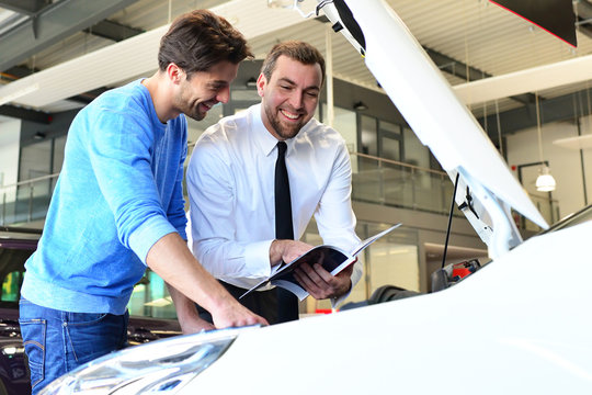 Sales at a car dealership - cheerful seller advises clients // Verkaufsgespräch in einem Autohaus - fröhlicher Verkäufer berät Kunden