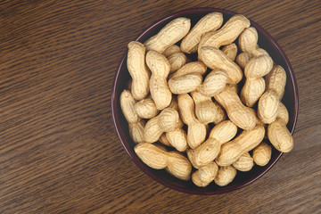 peanuts on a brown background in a ceramic bowl