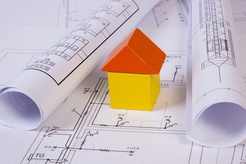 House of wooden blocks and rolls of diagrams on construction drawing of house