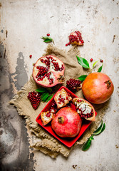 Pomegranates, whole and pieces in a Cup with leaves on the old fabric.