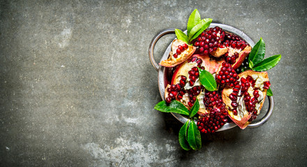 Ripe pomegranate with leaves in a saucepan. On stone table.