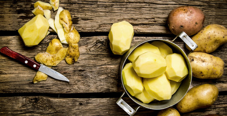 Peeled potatoes in an old pan with knife on wooden table .