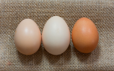 three raw chicken eggs in shell laid out in a row on the gunny, Close-up, top view