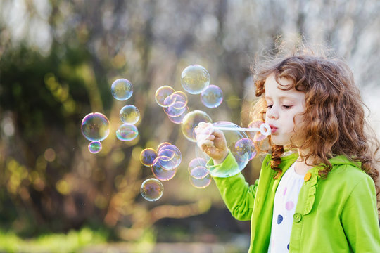 Cute girl blowing soap bubbles, closeup portrait.