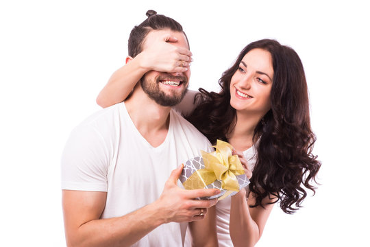Attractive happy woman with big toothy smile holding boyfriends eyes giving him a present for Valentine's day. Caucasian couple. White background.