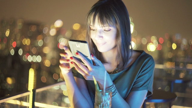 Young, pretty woman using smartphone in bar at night
