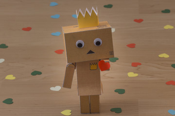 Ein kleiner Roboter aus Pappe mit einer Krone auf dem Kopf überreicht ein Valentinsherz