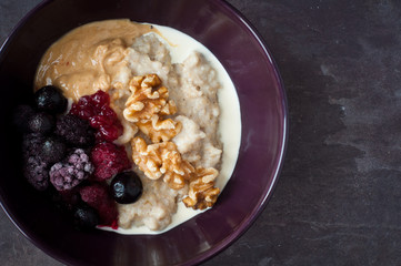 Bowl of oatmeal served on a stone slate table with frozen blackberries and raspberries. Topped with peanut butter and walnuts this is a healthy and nutritious breakfast.