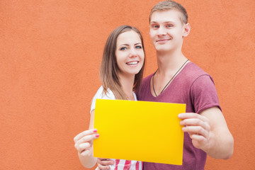 Happy couple looking at camera and holding yellow frame