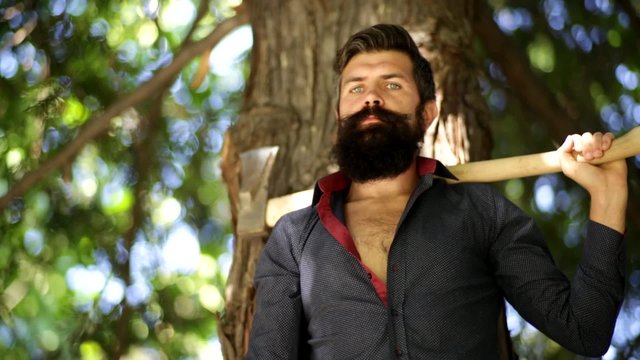 handsome man with blue eyes in the forest throws an ax on his shoulder