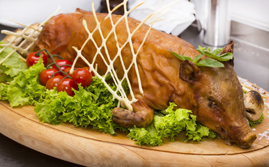 roasted suckling pig with vegetables on a wooden platter