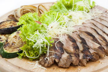 meat roasted on a grill with vegetables on a wooden plate