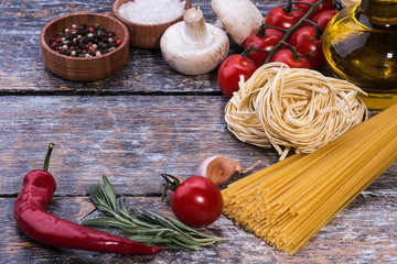 Ingredients for pasta, spagetti, tomatoes, olive oil, mushrooms on a wooden background