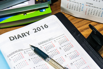 Diary planner book in black leather case and pen on the wooden t