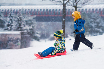 Two kids, boy brothers, sliding with bob in the snow, wintertime