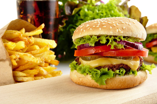 Cropped image of cheeseburger,french fries,glass of cola on wood