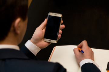 Man in business clothes with cellphone sitting at a table working on his notebook