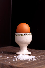 One brown egg lying on the dark Board with coarse salt.